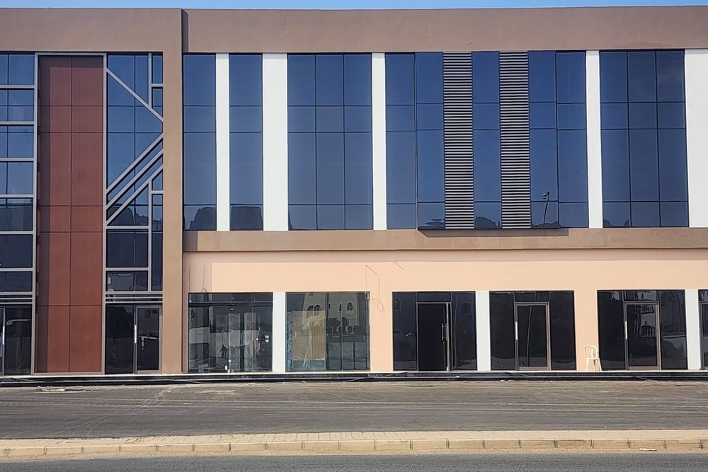 Al Ansab Plaza from the road: glazed shopfronts along the ground floor under a curtain-walled upper floor.